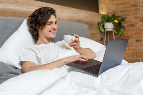 person having coffee on laptop in bed
