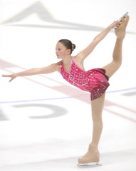 Image of cofounder of Algi, Alessandra Amato, figure skating in an ice rink wearing a pink dress. Her leg is up above her head, held in place by her hand as she glides across the surface of the ice.