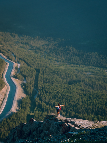 Girl hiking in Canmore and Banff Alberta Canada. Girl is standing on a rocky outcropping overlooking a valley filled with trees and wildlife.