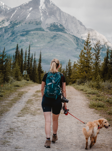 Girl hiking at the base of a mountain with a packed backpack and her dog in Canmore and Banff Alberta Canada