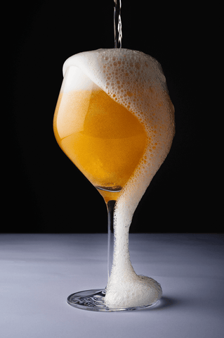 A glass of beer with foam running down the side in front of a black background