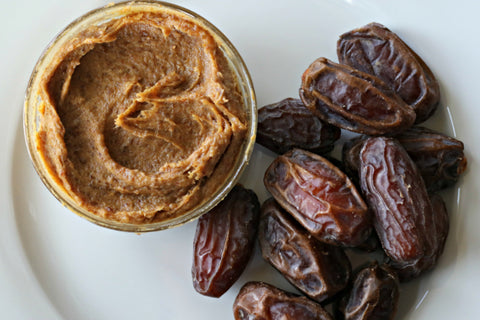 A glass jar of date paste beside a pile of medjool dates all sitting on a plate