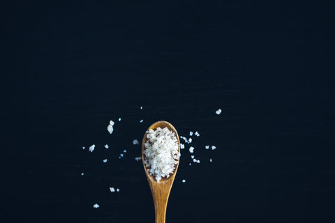 A wooden spoon filled with Medetarrenean sea salt crystal centred at the bottom of the image over a midnight blue background 