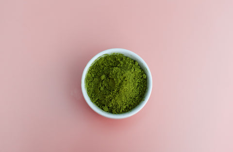 A white bowl of blue green spirulina algae centred on a pale pink background