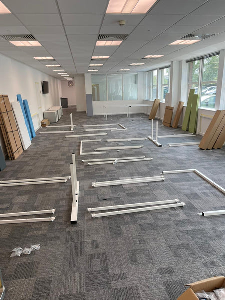 White frames of second hand bench desks laid out before assembly.