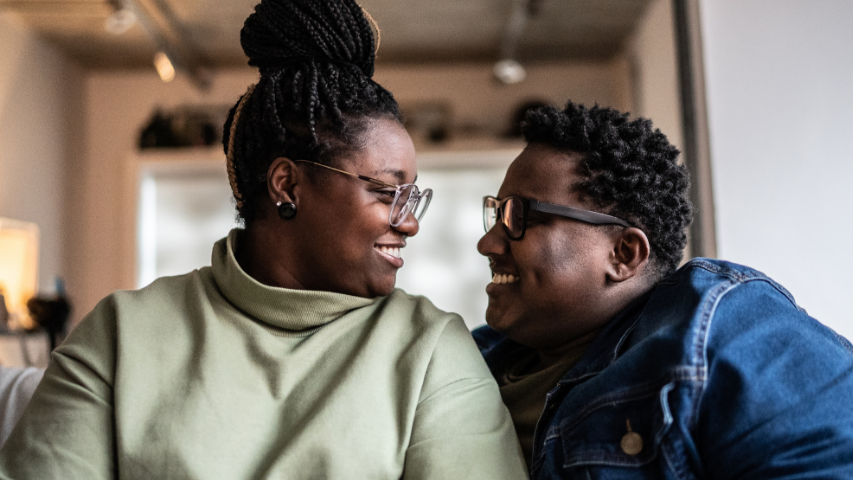 Couple wearing glasses smiling while looking at each other in the eyes on a sofa.