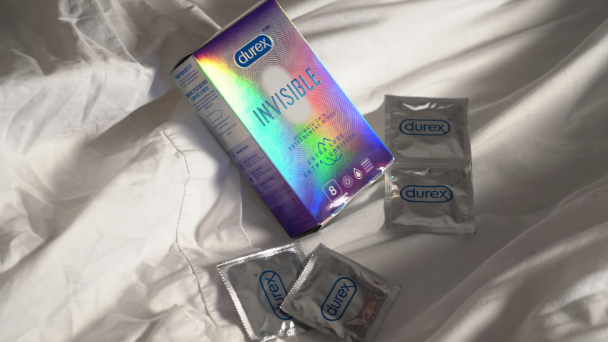 Des condoms extra lubrifiés Durex Invisible Extrêmement mince baignant dans la lumière du soleil sur des draps blancs.