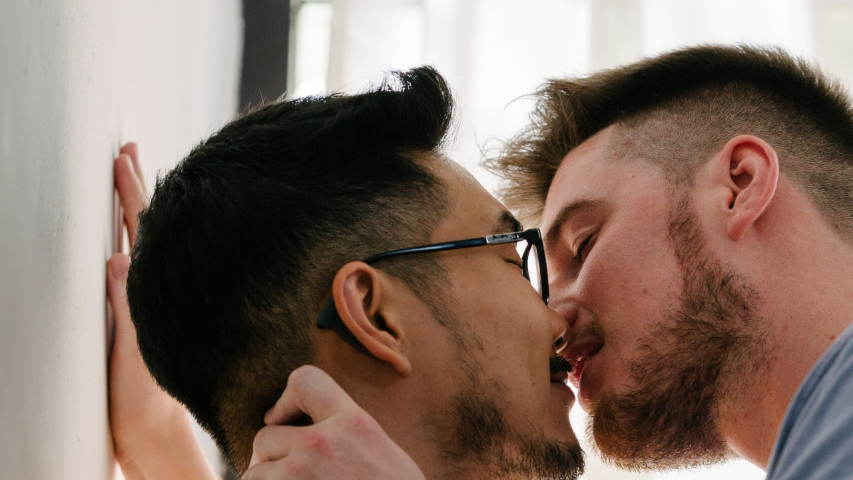 Two men sharing an intimate kiss up against a wall.