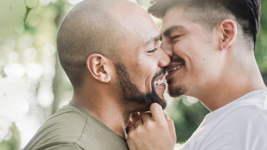 Two men sharing a lighthearted kiss after seeing each other again in person.