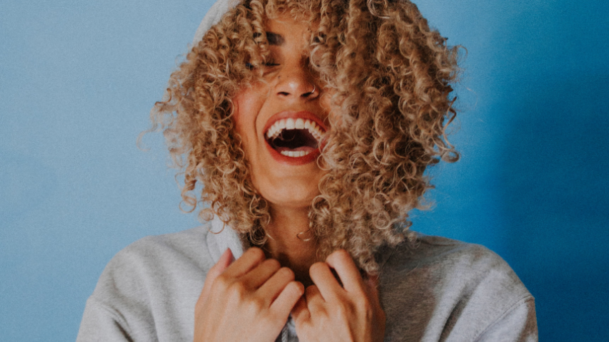 Curly-haired woman opening her mouth in delight while clutching her shirt