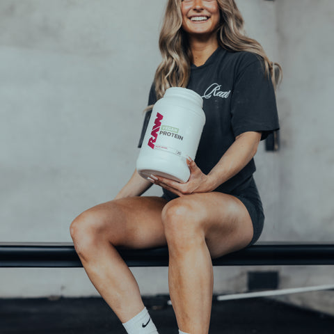 A female athlete holding a container of RAW Vegan Protein