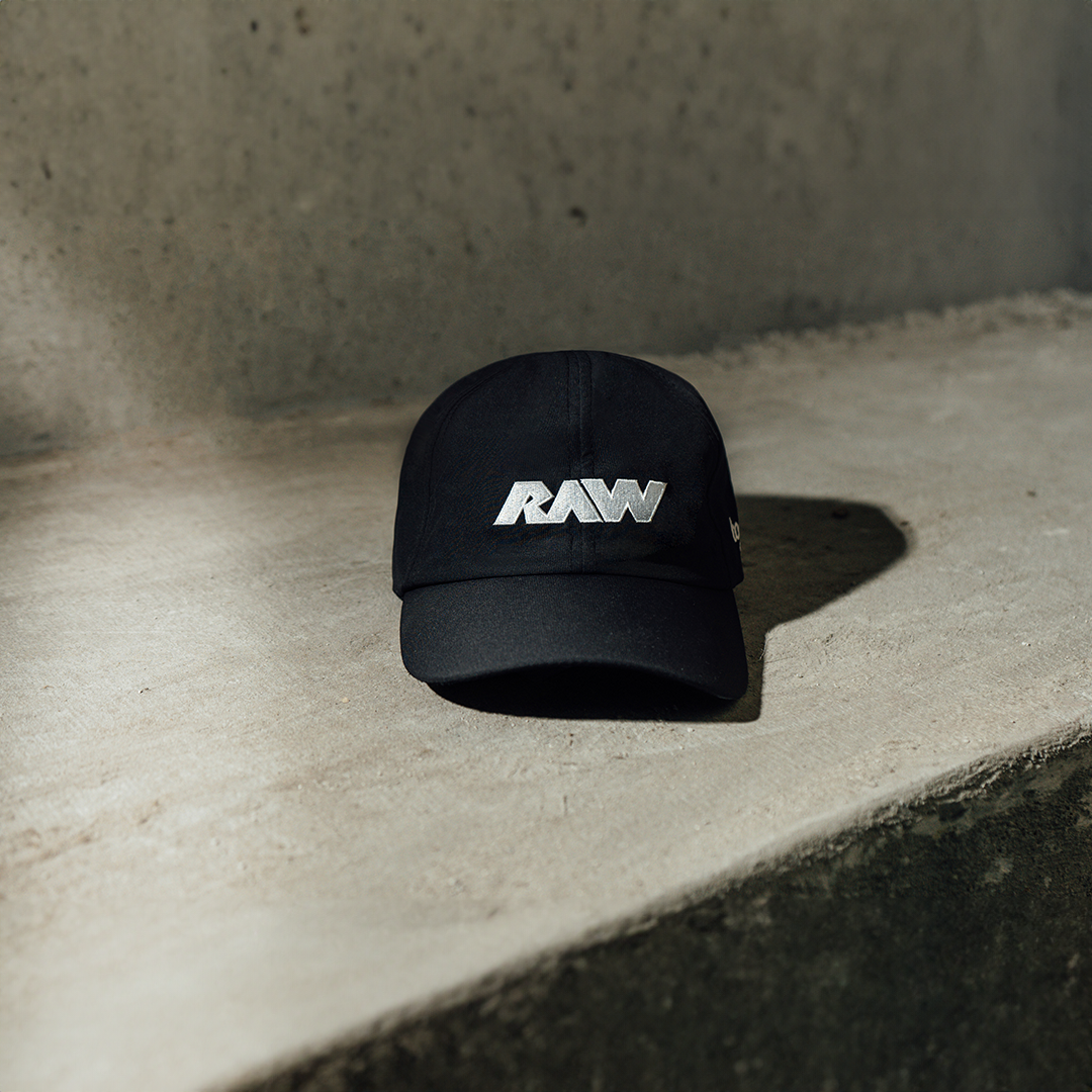 Black baseball cap with white 'RAW' logo on a concrete surface.