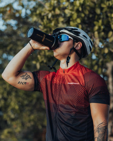 A man wearing a bicycle helmet and drinking from a water bottle