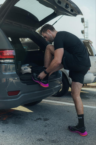 A man wearing a black t-shirt and shorts and tying his shoelace
