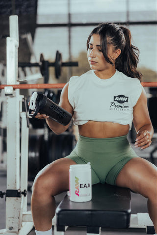 A woman sitting on a bench with a shaker bottle and RAW EAA