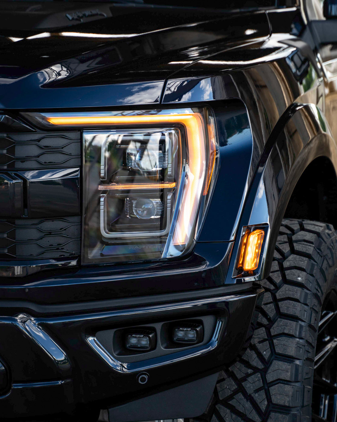 Close-up of a black truck's headlight and front grille with LED lights on.