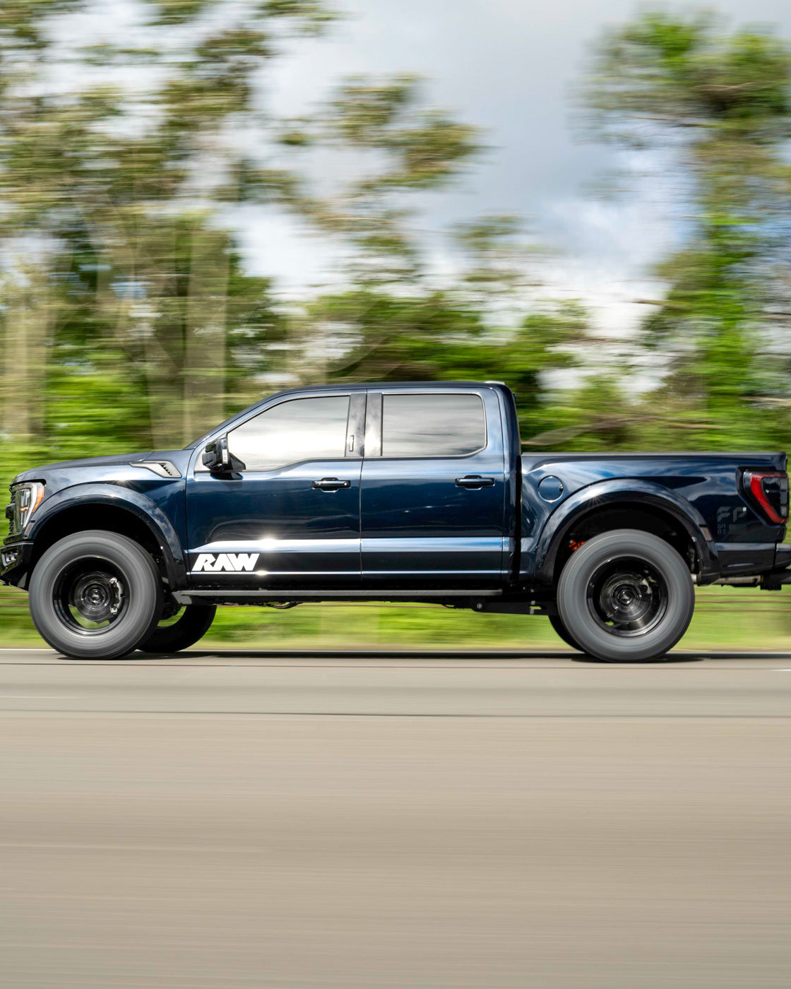 Blue pickup truck in motion on a road with blurred background.