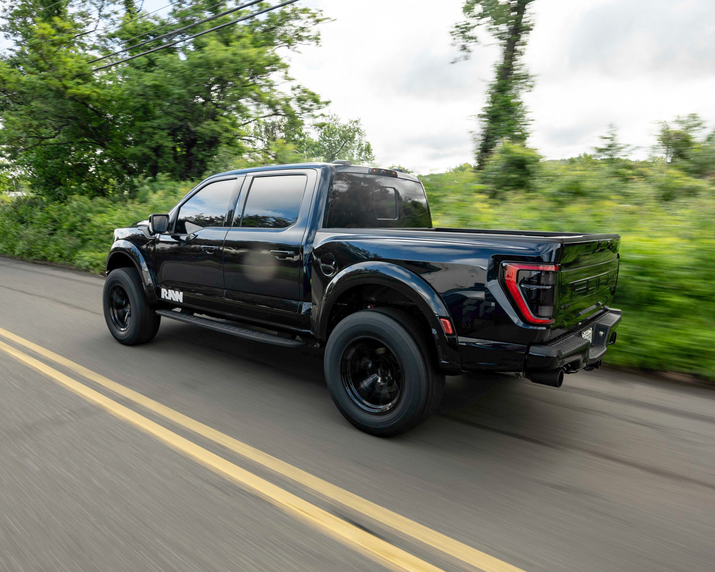 Black pickup truck driving on a road with greenery in the background.