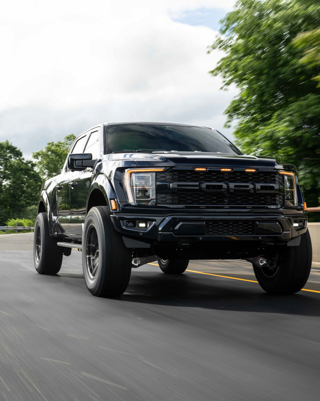 Black pickup truck driving on a road with trees in the background.