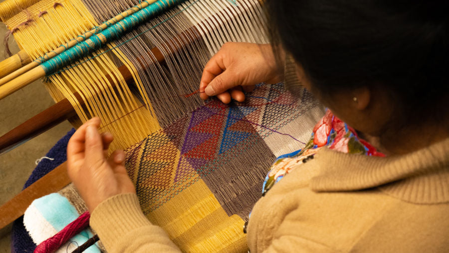 artisan woman weaving a colorful fabric by hand on a loom