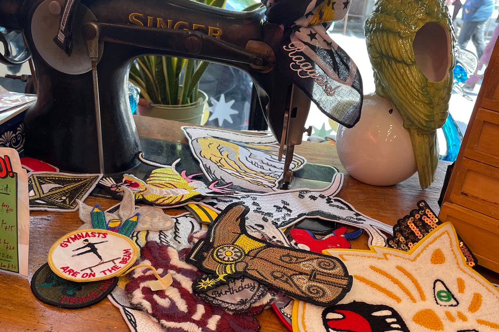 An array of different iron on patches strewn across a counter, alongside other vintage knick knacks and a Singer sewing machine