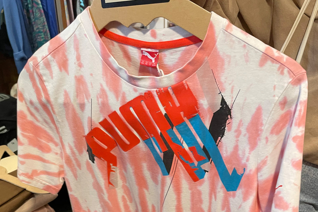 A pink and white tie dyed Puma t-shirt on a hanger.