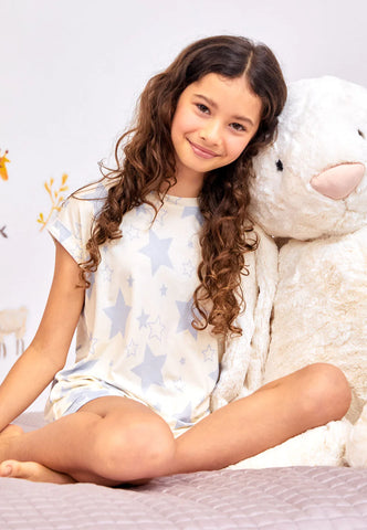 A young girl cuddled up to a large soft bunny toy in a bedroom, smiling happily at the camera wearing star print PJs.