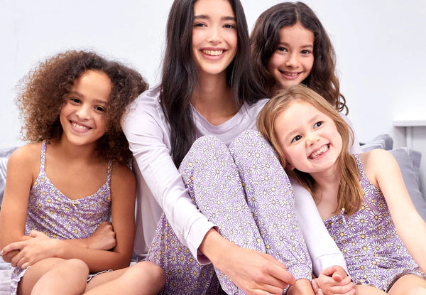 Three children cuddled up to a mum sitting on a bed, all wearing matching daisy print pyjamas and looking happy.