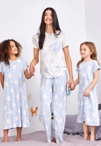 A mum holding hands with two girls standing on a bed looking happy, wearing matching star pyjamas and kids night dresses.
