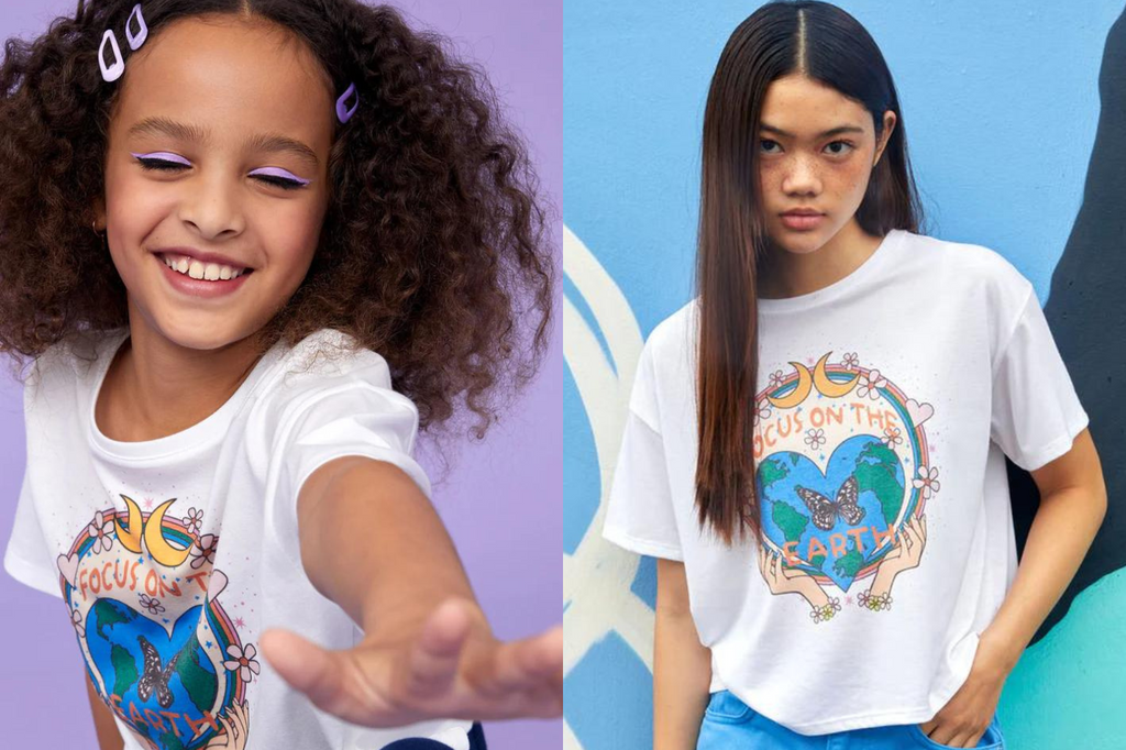 Two girls (Left: tween, eyes closed, brown curly hair pinned back with purple clips. Right: teen, long brown hair, eyes staring into camera) wearing Gen Woo’s ‘Focus On The Earth’ tee.
