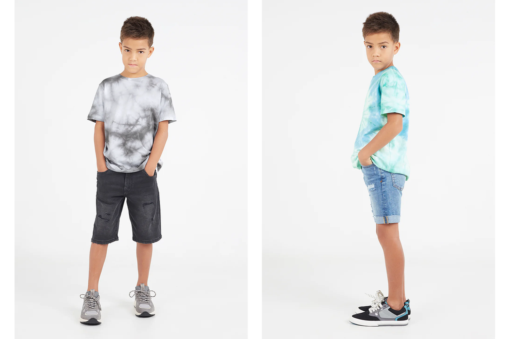 Young tween boy wears varying tie-dye t-shirts by Gen Woo, styled with denim shorts and sneakers.