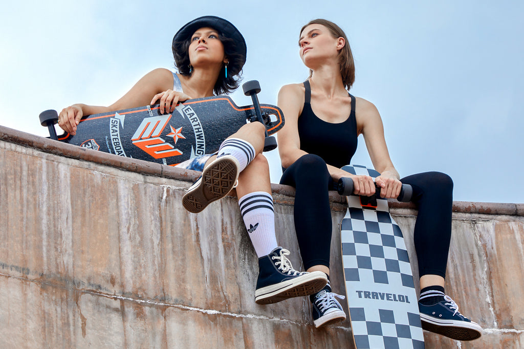Two women sat on the edge of a skate bowl, looking out to the distance. Styling skate clothes by Gen Woo and thoughtfully holding their skateboards.