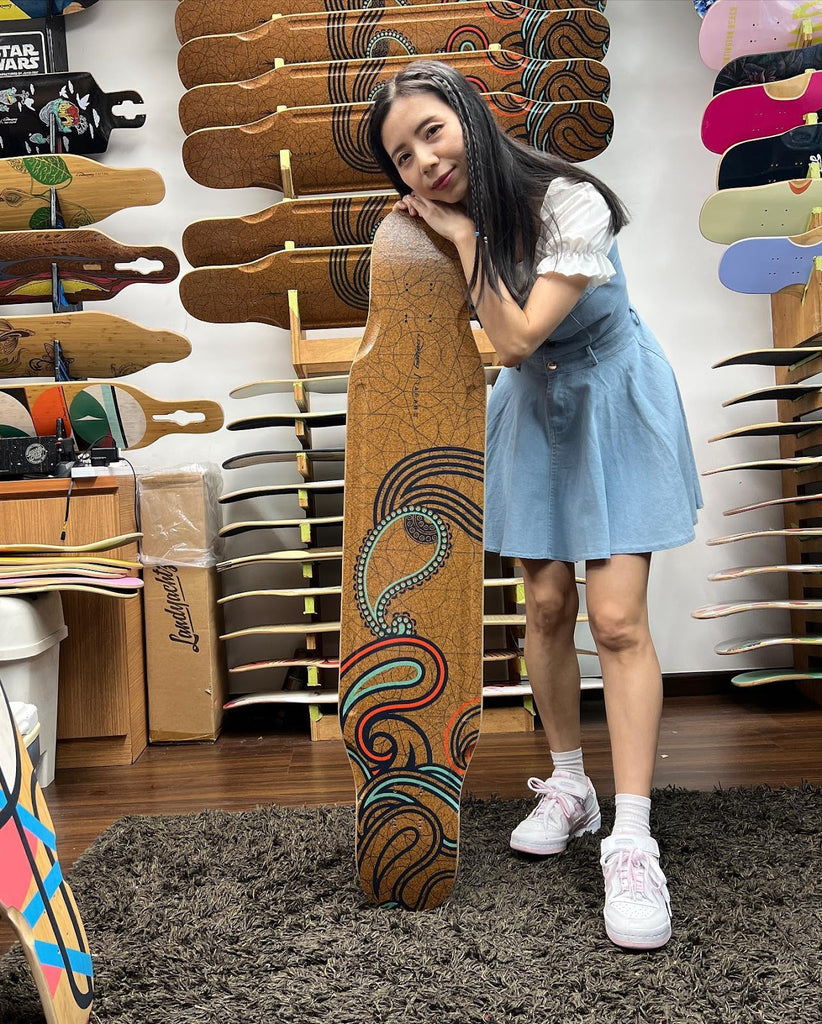 Skateboarding influencer contentedly leans on a longboard in the Singapore Longboard Love skate shop.