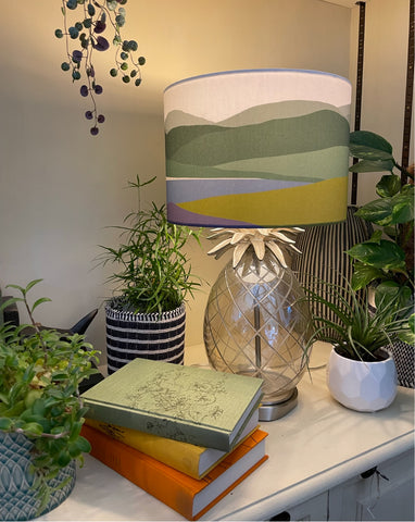 Lampshade on glass pineapple lamp base from Laura Ashley. Drum lampshade features our Welsh Hills Heather and Gorse design in greens and purples.