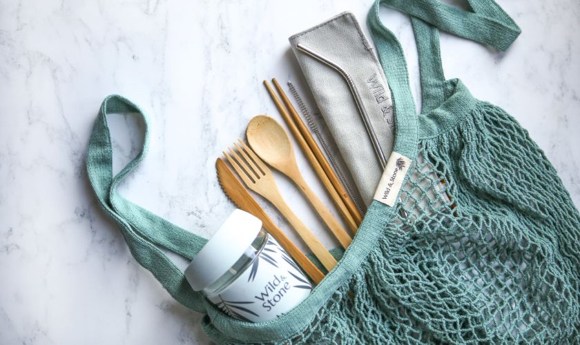 reusable beach bag filled with essentials, such as a reusable cup and bamboo cutlery 