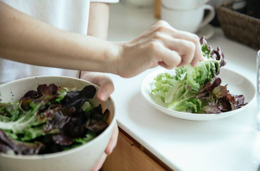 Person putting salad into plate from bowl