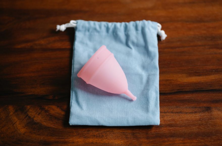 A pink menstrual cup sitting on a blue cotton pouch.