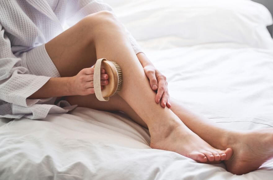 Woman body brushing on a white bed