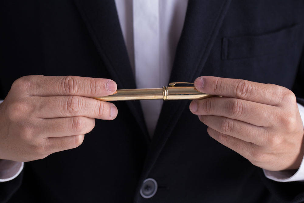 A man in black casual suit giving a gold fountain pen