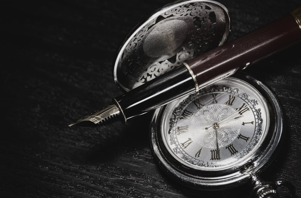 Beautiful pocket watch and fountain pen close up on a black wooden table