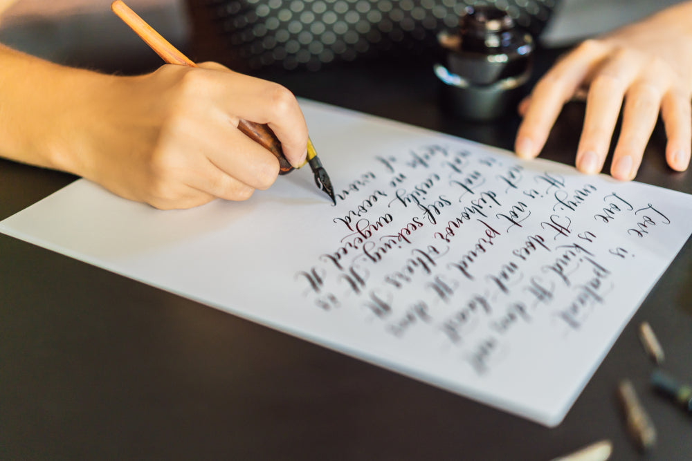 Calligrapher hands writes phrase on white paper