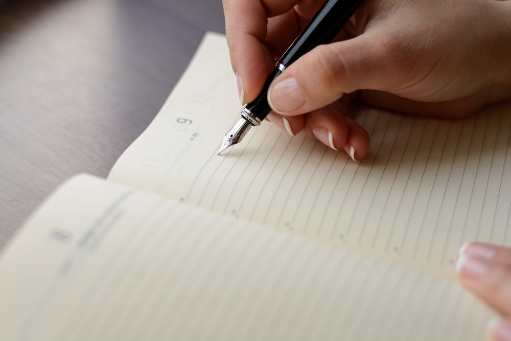 Female hand writing in notebook with pen.