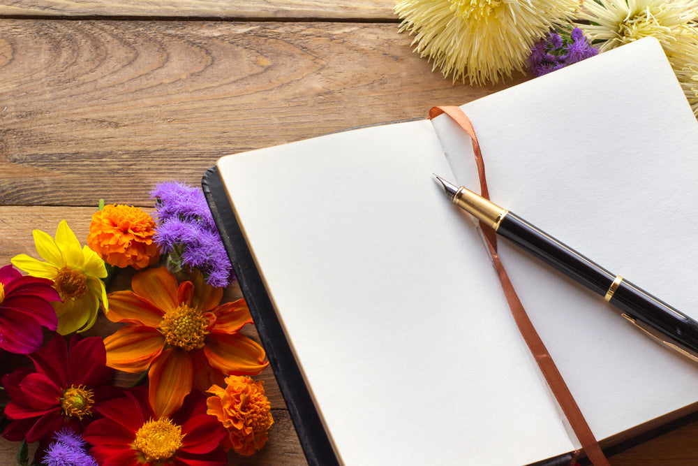 Floral arrangement on a wooden background with an open notebook in the center and a fountain pen lying on the pages.