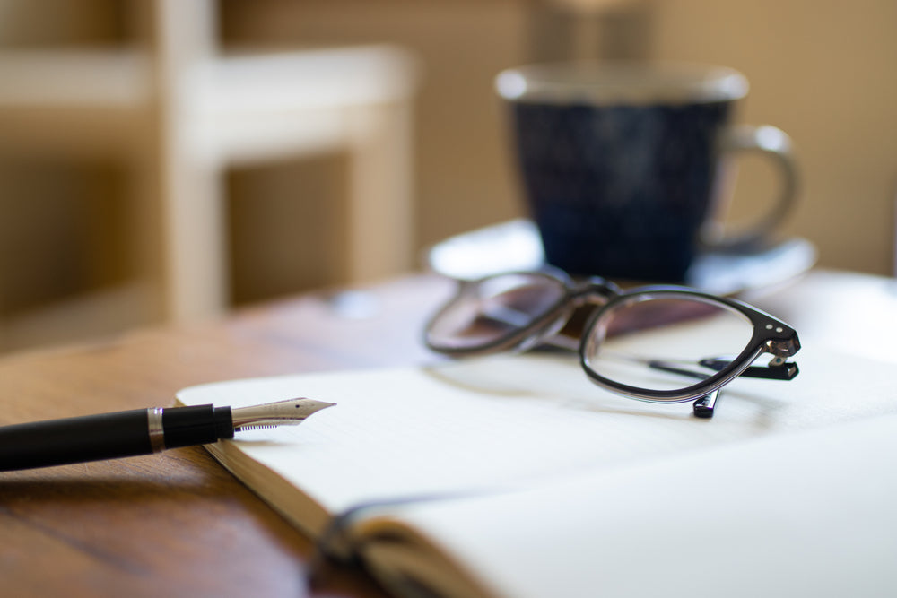 Journal entry with ink fountain pen glasses, coffee cup and desk background.