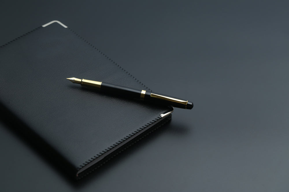 golden pen,notebook,calculator and glasses on black desk