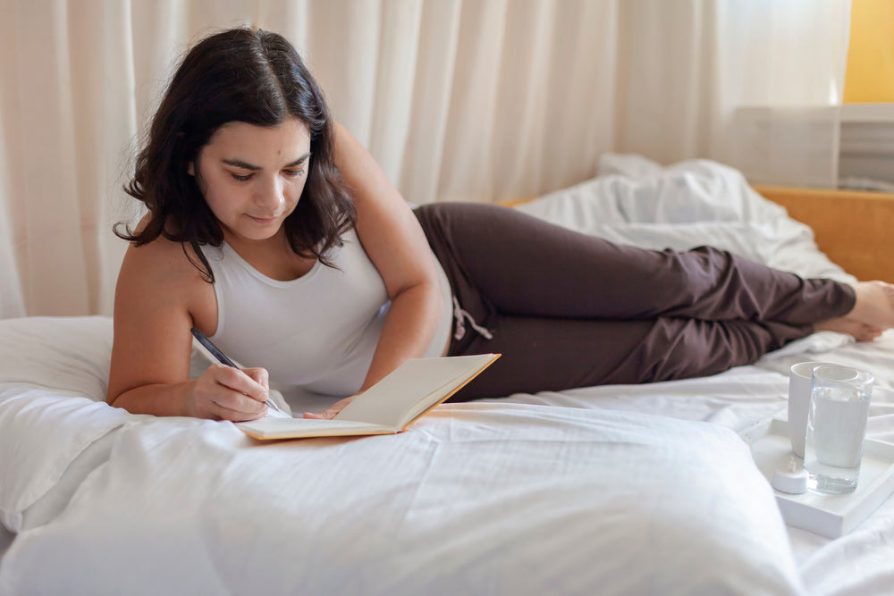 woman lying in bed, practicing stress relief challenge with journal 