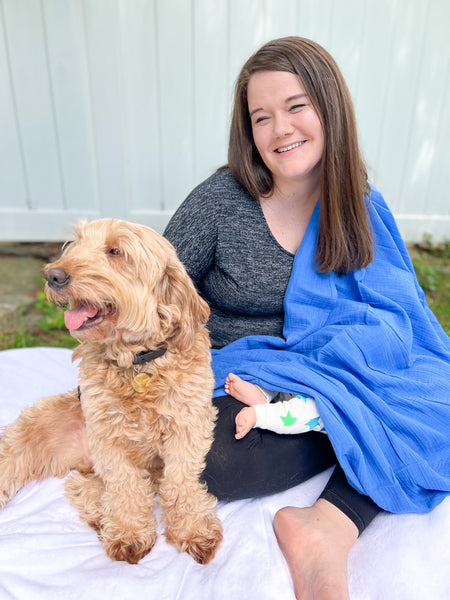 goldendoodle sitting next to woman using muslin swaddle blanket as nursing cover
