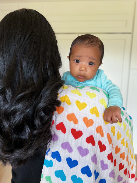 woman holding baby wearing mint pajamas using rainbow heart swaddle 