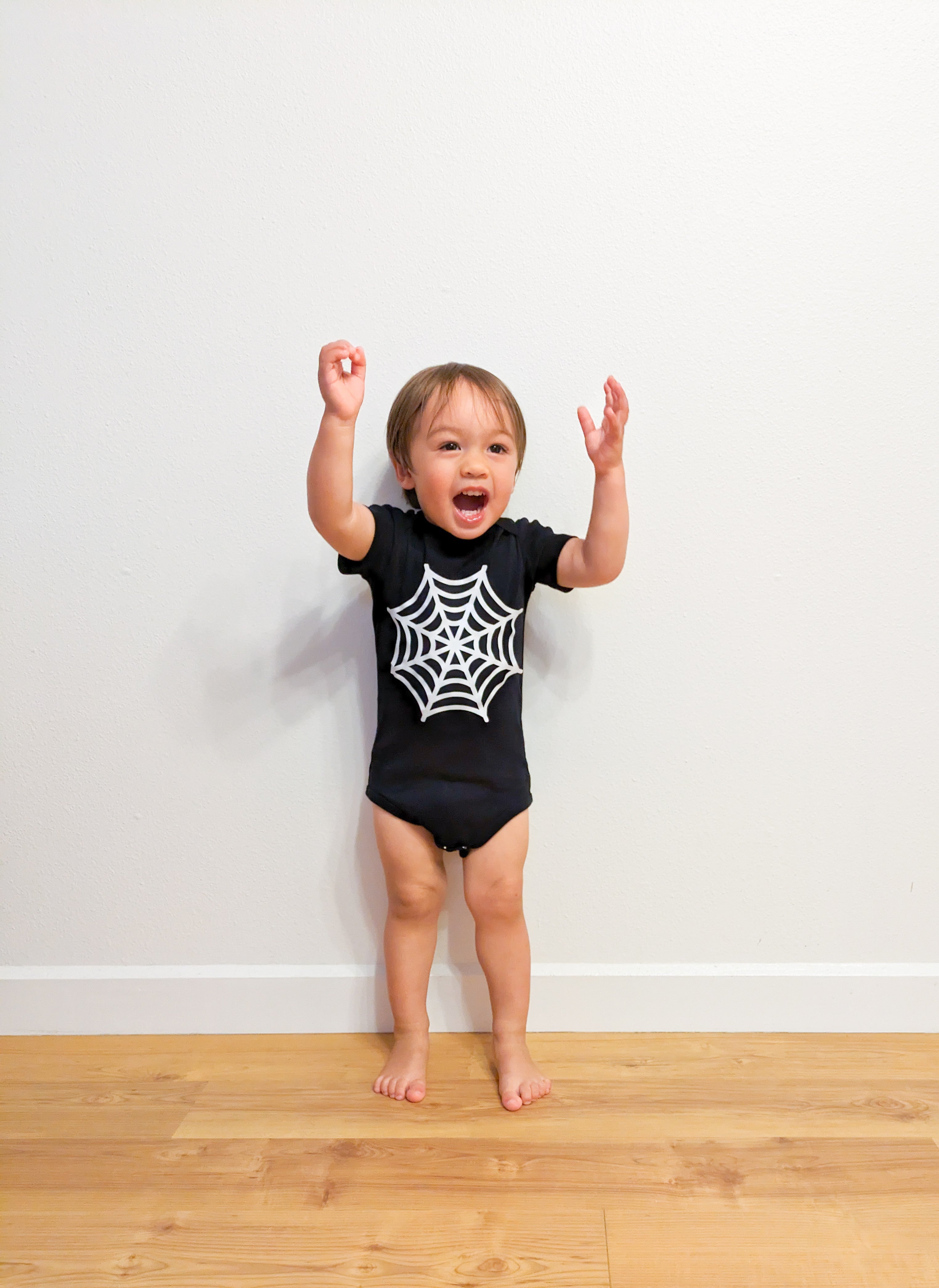 A baby wearing a black bodysuit with a DIY spiderweb painted on the chest