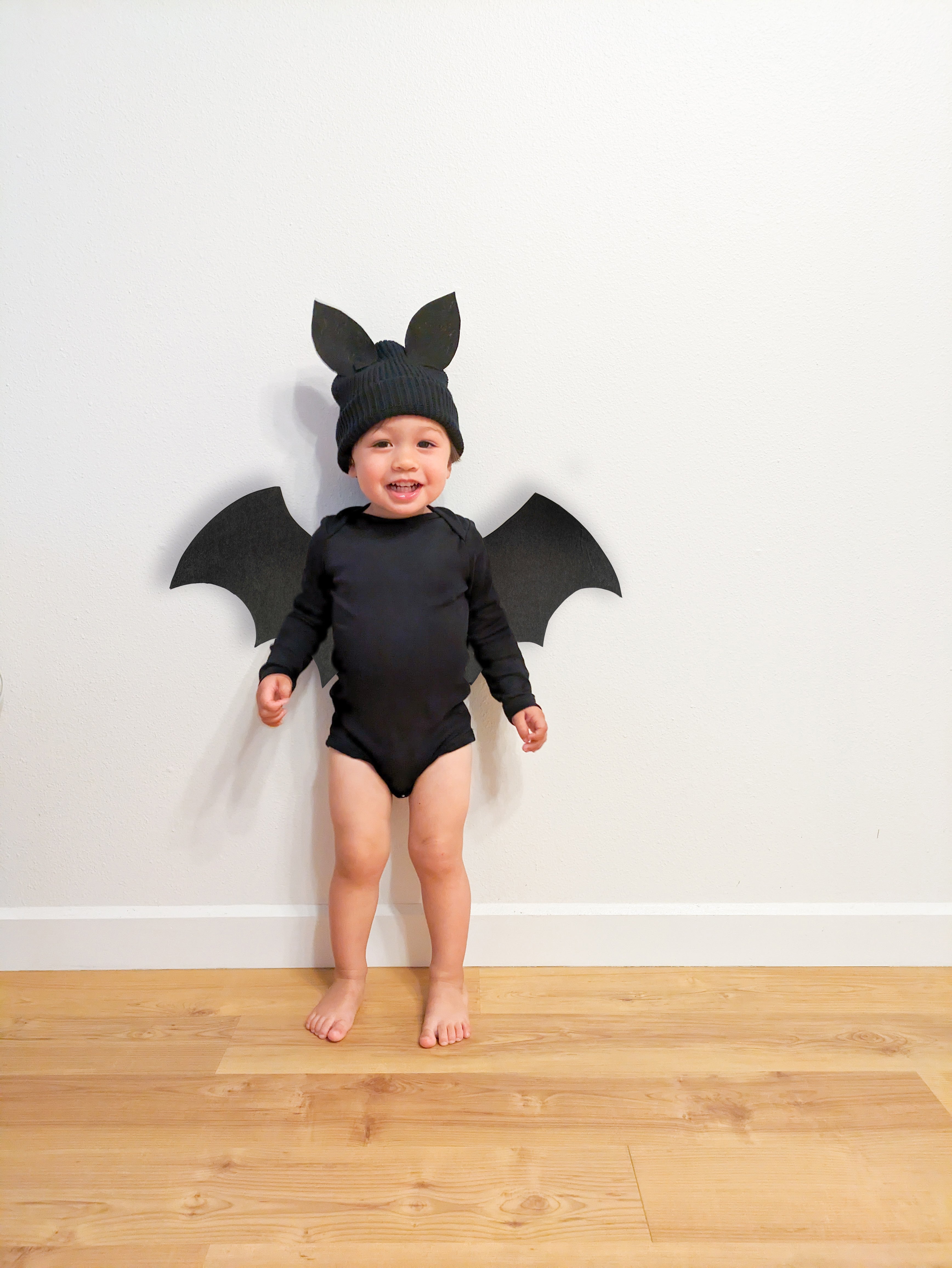 A toddler dressed in a DIY black bat costume with homemade bat wings and a black bodysuit